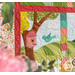 Close up of one block from the "Welcome Home in Spring" quilt showing a tree holding a pink birdhouse, a teal bird flying home toward it; pink flowers are visible in the foreground.