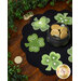 The completed mat from a slight angle, staged on a rustic cherry wood table and surrounded by a green garland and tossed golden coins.