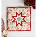 A shot of just the square hot pad, staged on a white paneled counter with deep red flowers and a red whisk.