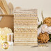 A stack of neatly arranged fabric rolls in various shades of cream and beige, some with decorative patterns and embellishments. In the foreground, there are spools of thread, a pair of scissors, and a bouquet of flowers.