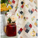 A close up of a playful beige quilt with colorful blocks with planters of flowers in the foreground