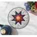 A top down shot of the round hot pad, staged on a white table top with coordinating flowers and a navy blue teapot.