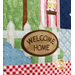A super close up on the sign that reads "Welcome Home" on the white picket fence of the quilt, demonstrating fabric and topstitching details.