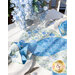 A beautifully set dining table featuring a floral tablecloth with blue and white patterns, adorned with blue table napkins folded elegantly. A vase filled with blue flowers sits in the center, complementing the decor.