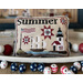 A decorative cross stitch pillow features a nautical theme with a ship, lighthouse, stars, and flags, labeled Summer.