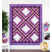 A shot of the full and completed Irish Chain quilt in bright purples, pinks, and white, hung on a white paneled wall and staged with coordinating furniture and decor.