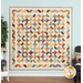 The completed Garden Path quilt colored in Gift of Grateful Praise, a rainbow of vibrant earth tones. Hung on a blue paneled wall, the quilt is staged with coordinating furniture and matching decor.