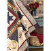 A shot of the draped quilt, focusing on the right side of the quilt. A coordinating dusty teal nightstand is staged with the quilt, holding a basket with a red blanket and a pot of red and yellow roses.