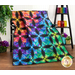 The completed Pineapple quilt in a rainbow of colors and prints, artfully draped over a black bench and staged with coordinating rainbow decor like fabric, jars, and flowers.