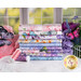 A stack of the fabrics in the Secret Garden collection, with flowers and butterflies and thread.