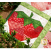 A super close up on a red strawberry, demonstrating piecing and topstitching details. A green garland frames the bottom of the wall hanging.