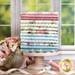 A stack of pink, cream, and blue fabrics in the Just Rosy collection, with flowers, thread, ribbon, and a bird statue.