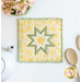 A top down shot of the completed square hot pad in yellow, staged on a white table with coordinating decor like flowers, a white teapot, and wooden spoons.