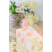 A shot of one of the mini charm bags staged on a light wooden countertop with a pink pot of yellow flowers, showcasing the pink tabs on either end of the bag.