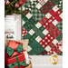 A close up on the bottom corner of the picnic quilt, showing fabric and stitching details. In the foreground, a stack of presents sits in a basket, with coordinating Christmas decor along the left side of the frame.