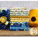 A stack of yellow, blue, and cream fabrics that are in the Bee & Bee Kind FQ set, with flowers and a ceramic beehive.