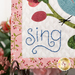 A super close up on the hand-embroidered word "Sing" of the quilt, also demonstrating fabric details.