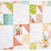 A colorful quilt featuring various geometric patterns and floral designs in shades of green, pink, and orange on a white background, showcasing intricate stitching.