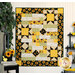 The completed Comfort of Psalms Quilt, colored in bold yellow, black, white, and green fabrics from the Sunflower Splendor collection. The quilt is displayed on an off-white paneled wall and staged with coordinating Sunflower themed decor.