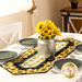 The completed table runner on a white table showing detail on the sunflower and butterfly fabrics and staged with coordinating plates, glassware, and a tin holding decorative sunflowers.