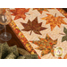 A top view of the table runner, demonstrating fabric and top quilting details. A wine glass and plate set with an Autumn Celebration fabric napkin sit at the left side of the frame.