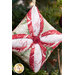 A super close up on one of the completed ornaments, colored in cream, red, and sage green fabrics and staged in front of a lit Christmas tree, showing details on the center button.