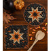 Two quilted hot pads, one round and one square, featuring a star design in orange and black displayed on a wooden table with coordinating seasonal decor.