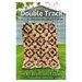 The front of the Double Track pattern featuring the finished quilt being held up by someone in front of a metal shed in a backyard.