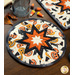 An angled top shot of the completed round hot pad in cream, staged on a wooden table with coordinating decor like autumn leaves and candy corn.