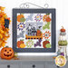 The completed Midnight Manor wall hanging, hung on a white paneled wall and staged with coordinating pumpkins and Halloween decor.