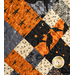 A super close up on the criss cross design of the picnic quilt in black, gray, orange, and cream, showing fabric and stitching details. Stitched pumpkins can be seen across the fabric.