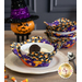 A vibrant fabric bowl cozy filled with dessert, surrounded by decorative Halloween items and a stack of three other matching bowl cozies.