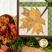 A close up on the lower left hand corner of the project with a golden maple leaf, demonstrating fabric and piecing details. Coordinating decor peeks into frame from the left side.