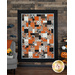 The completed Easy As ABC and 123 Quilt in P&B Textiles' Witching Hour collection hung on a brown paneled wall with warm orange decor on either side of the quilt.