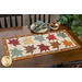 A colorful autumn-themed table runner staged on a wooden dining table and staged with plates and decor in the corner.