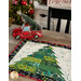 A close up on one of the green trees of the runner, demonstrating fabric, piecing, and top quilting details. A decorative red truck with a tree in the bed sits beside the runner on a rustic wood table.