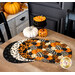 The four completed Oval Placemats colored in black, cream, and orange fabrics from the Hallow's Eve collection, slightly fanned out and staged on a wooden table, surrounded by coordinating tableware and Halloween decor.