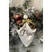 A decorative wreath featuring a white fabric angel ornament with Peace printed on it, adorned with pine and ornaments.