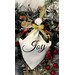 A decorative angel ornament with the word Joy on a white fabric, surrounded by festive greenery and berries.