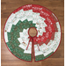 Round Christmas tree skirt featuring alternating red, green, and white patterned fabric pieces on a wooden background