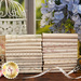 A  photographed image of the fabrics in the Pebbles FQ set stacked on a brown wooden table with coordinating flower arrangements and decor.