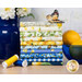 A stack of the fabric featured in the Limoncello FQ set, with lemons in a bowl and a vase and flowers and thread and a butterfly