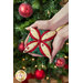 A model holds one of the cathedral ornaments in cream, red, and green with a decorated Christmas tree in the background.