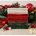 A stack of the fabrics included in the Tonga Mistletoe FQ set, with a holiday garland and ornaments and presents and thread.