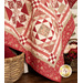 A close up on a corner of the draped quilt, staged with a red blanket in a basket and a basket of coordinating flowers.