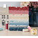 A stack of the fabrics included in the Cozy House FQ set, with a vase and flowers and thread and a house decoration.