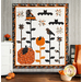 The completed Halloween Garden quilt in white, black, and orange, staged on a gray paneled wall with coordinating decor.