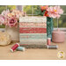 A stack of the fabrics included in the Muse Fat Quarter set, with flowers and vases and thread.