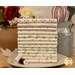 A stack of the fabrics included in the Buttercream & Brickle Bits FQ set, with a jug and a vase and a whisk and spatula and flowers and thread and a plate.