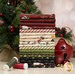 A stack of the fabrics available in the Naughty or Nice collection, with a tree and a festive bell and ornaments and thread.